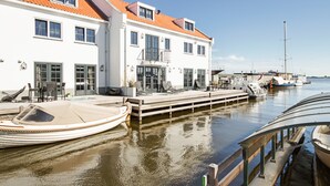 A waterfront property with a dock, a covered boat, and a building with multiple windows and balconies. - Najade Hotel (Loosdrecht)