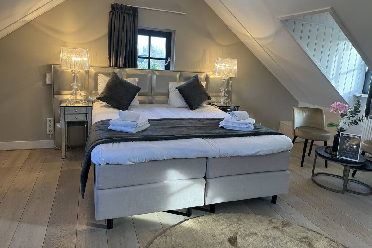 A modern bedroom with a large bed, two bedside tables, a chair, and a small table with a vase of flowers.