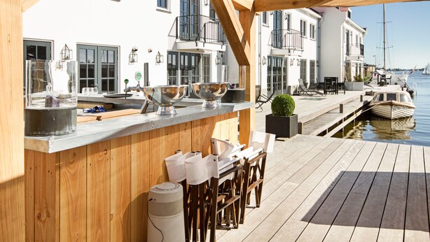 A waterfront bar with wooden seating, a bar counter, and a view of the water. - Najade Hotel (Loosdrecht)