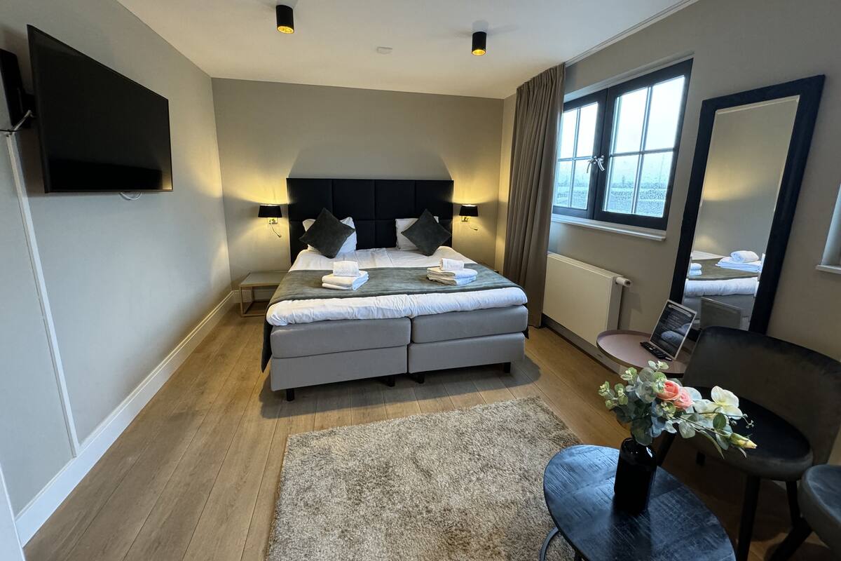 A modern bedroom with a large bed, bedside lamps, a flat-screen TV, a desk with a chair, and a window with curtains.