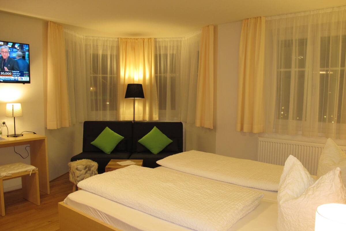 Een hotelkamer met twee bedden, een televisie aan de muur, een lamp en een raam met gordijnen.