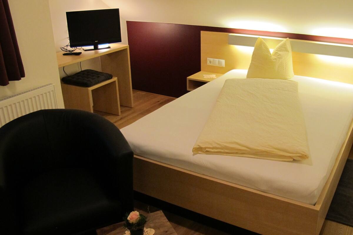Hotelkamer met een bed, een bureau met een computer, een stoel en een tafeltje met een bloem.