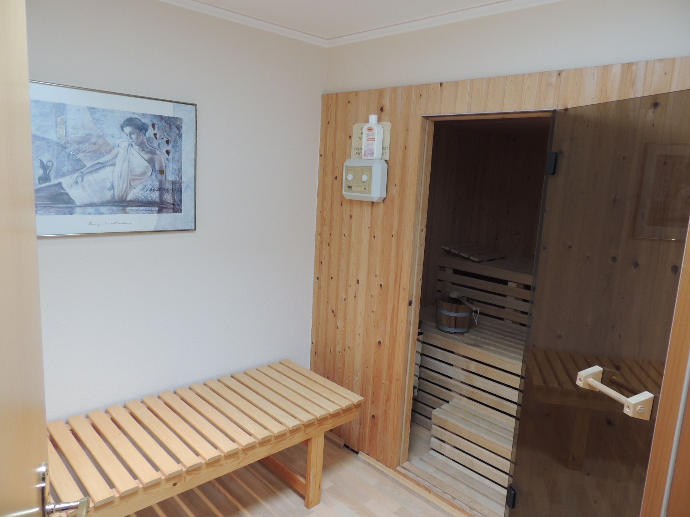 Un cuarto de sauna con un banco de madera, una puerta de madera y un panel de control en la pared.