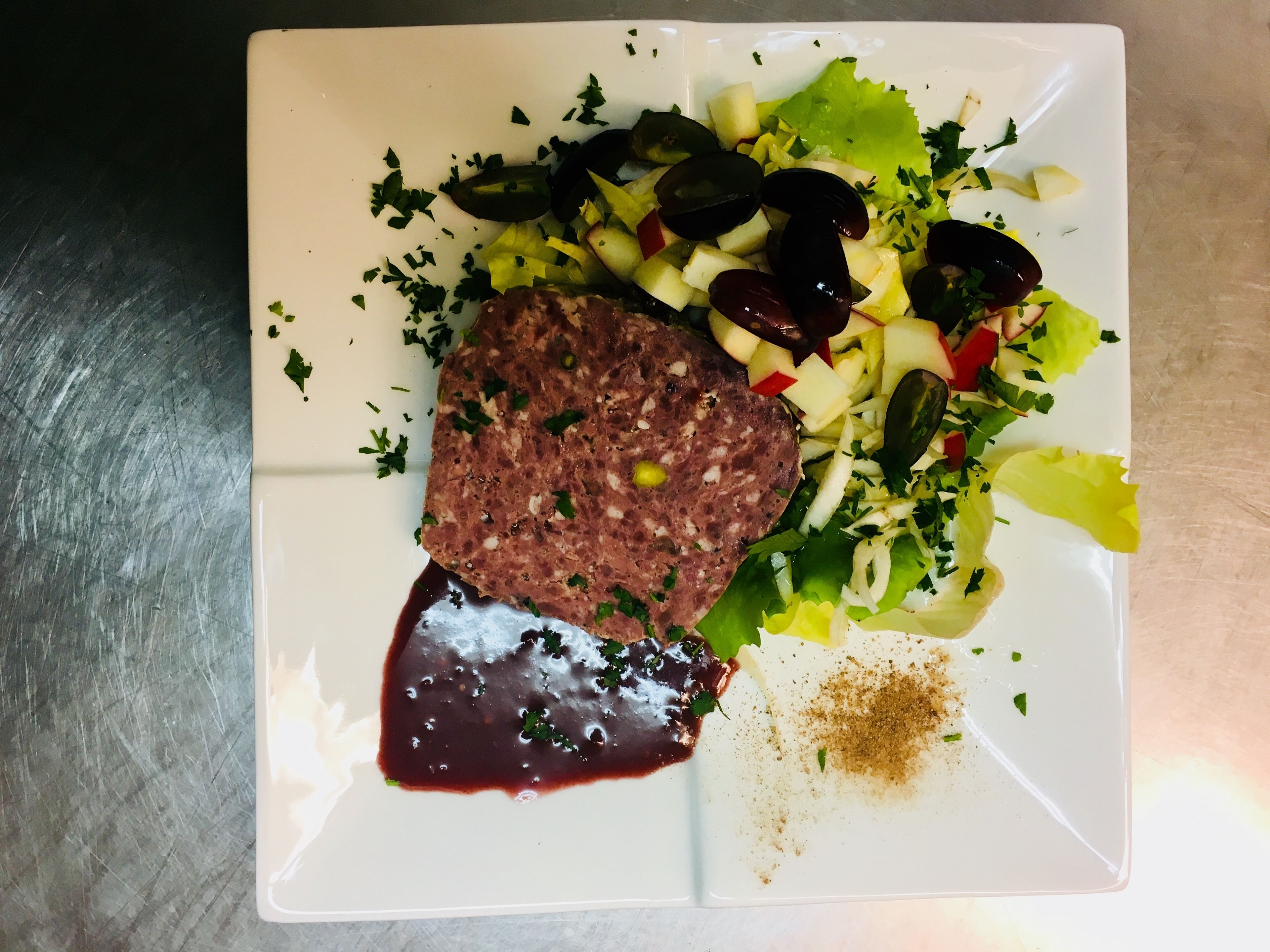 A plate with a meatloaf, salad, and a dark sauce.