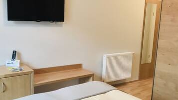 A hotel room with a bed, a desk, a chair, a television, and a radiator.