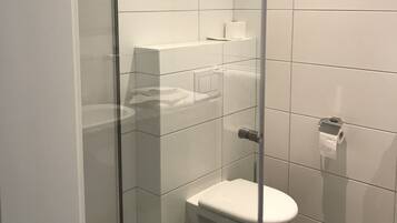 A modern bathroom with a glass-enclosed shower, a toilet, and a shelf with a roll of toilet paper.