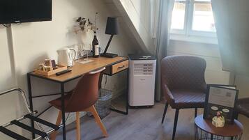Una habitación de hotel moderna con un escritorio de madera, dos sillas, un televisor de pantalla plana, un mini refrigerador y una ventana con cortinas.