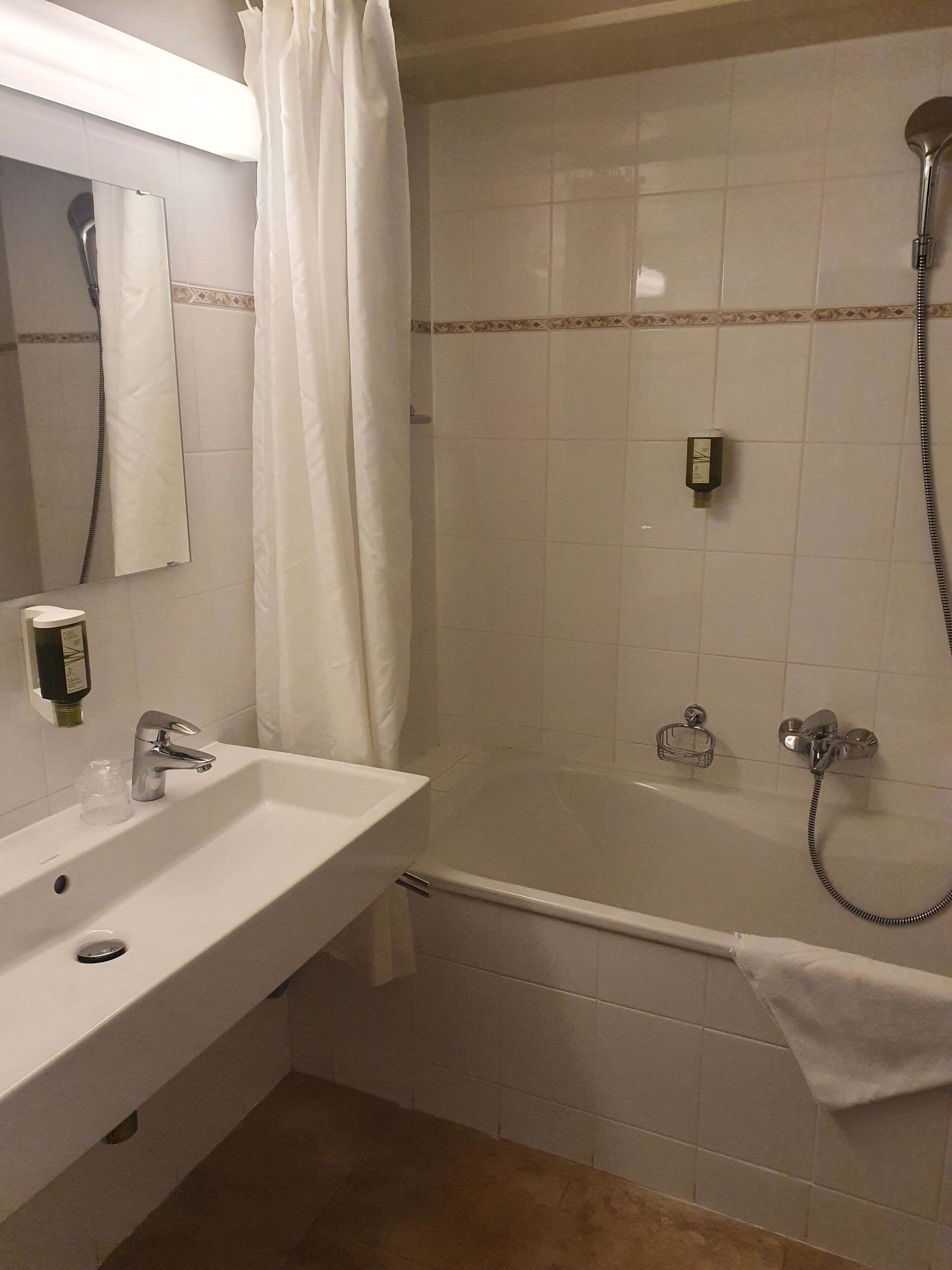 Un baño con lavamanos, espejo, ducha y toallero.