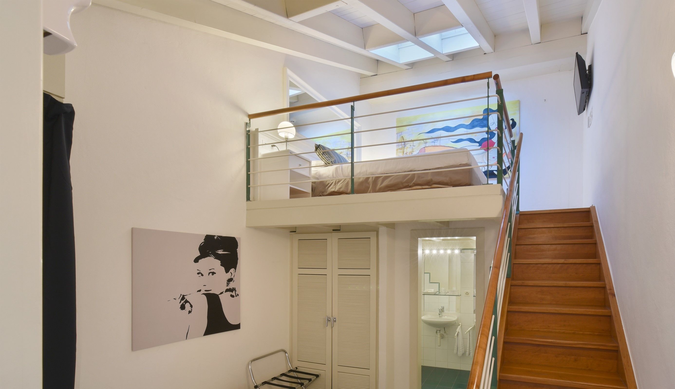Un dormitorio tipo loft con una cama litera, una escalera, un baño con lavamanos y un cuadro en la pared.