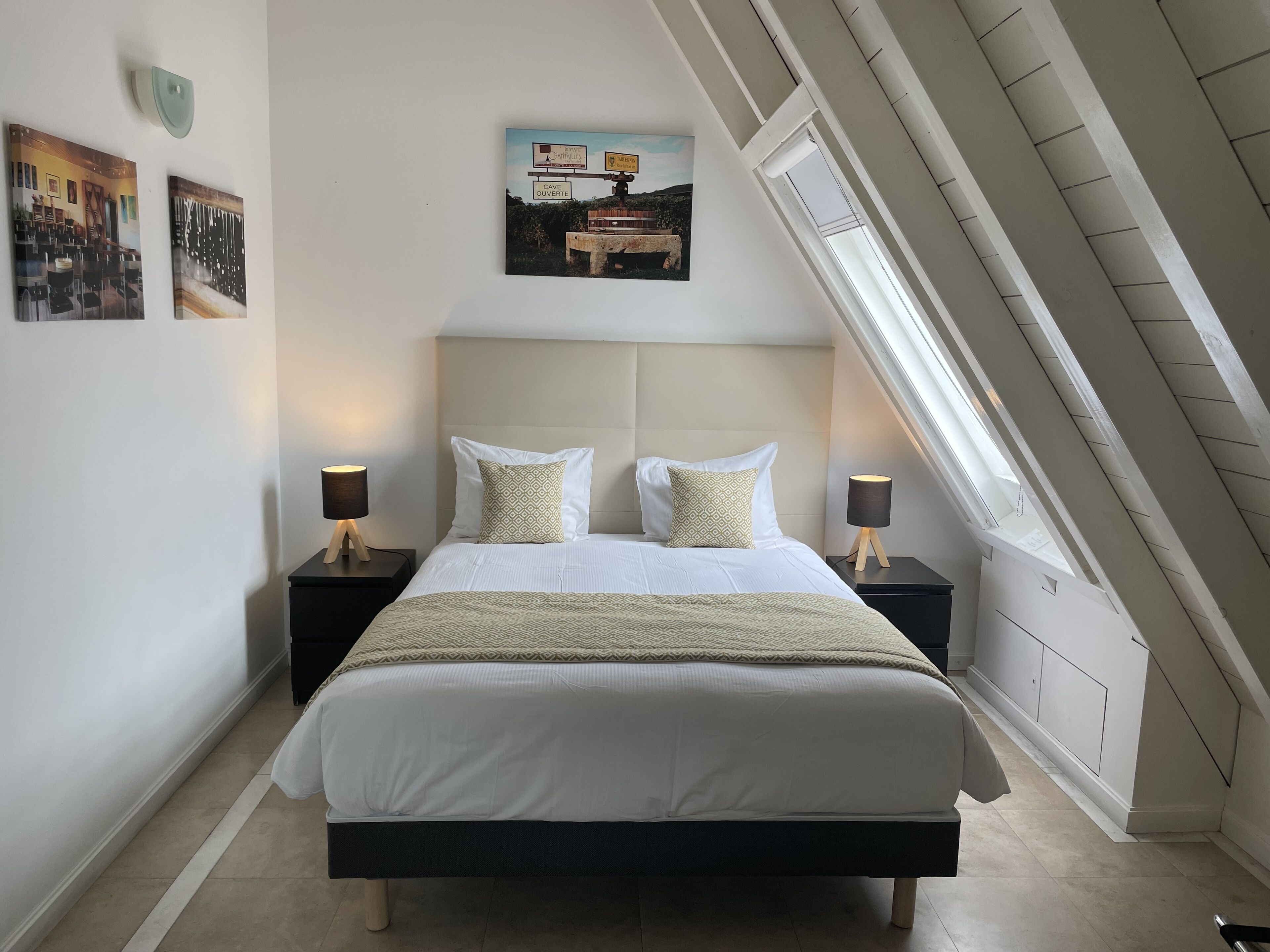 A bedroom with a bed, two nightstands, a wall-mounted picture, and a skylight.