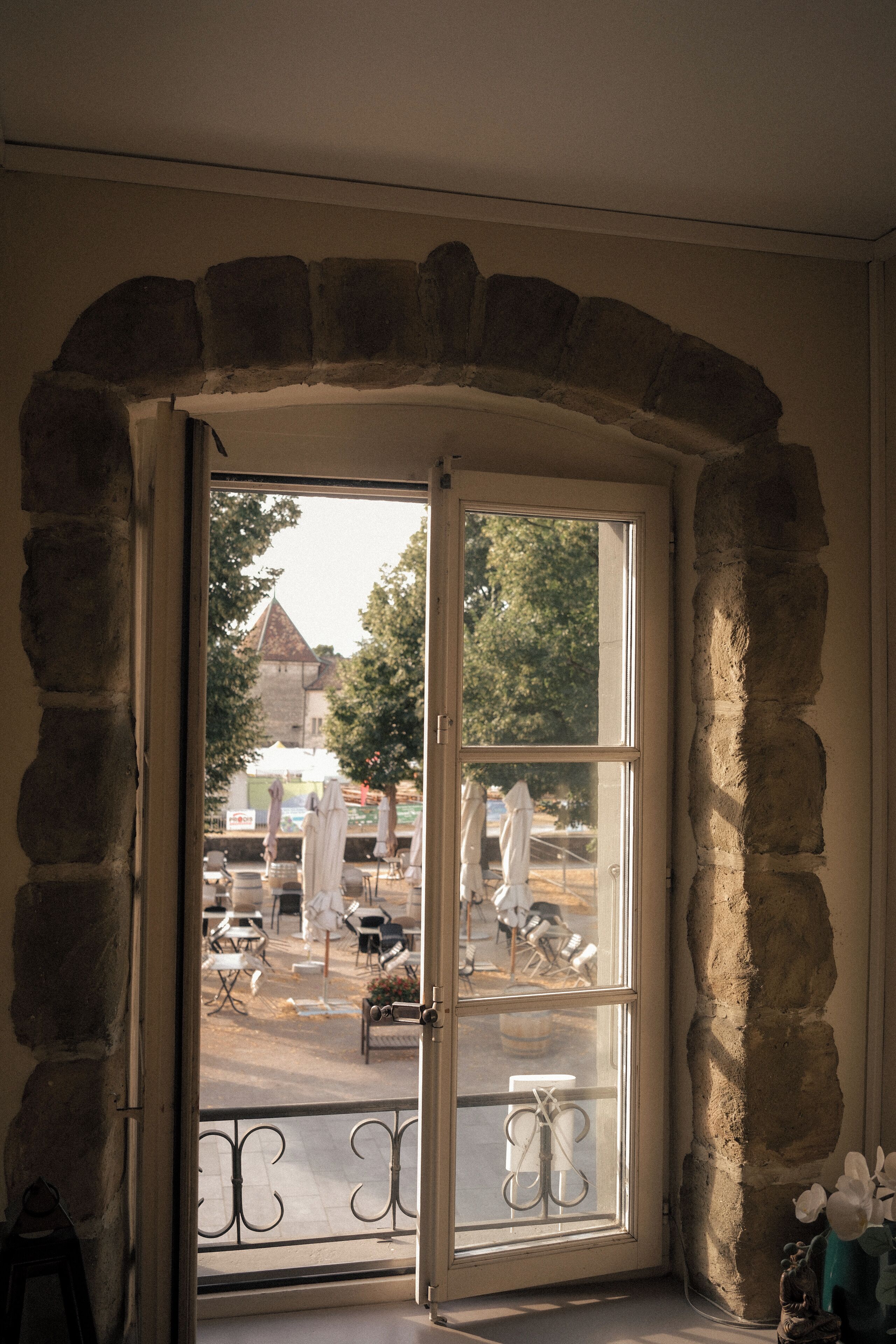 A stone-framed doorway leading to an outdoor area with tables and chairs, a building with a pointed roof, and a statue.