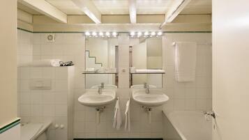 Un baño con dos lavamanos, un inodoro, una bañera y un espejo sobre los lavamanos.