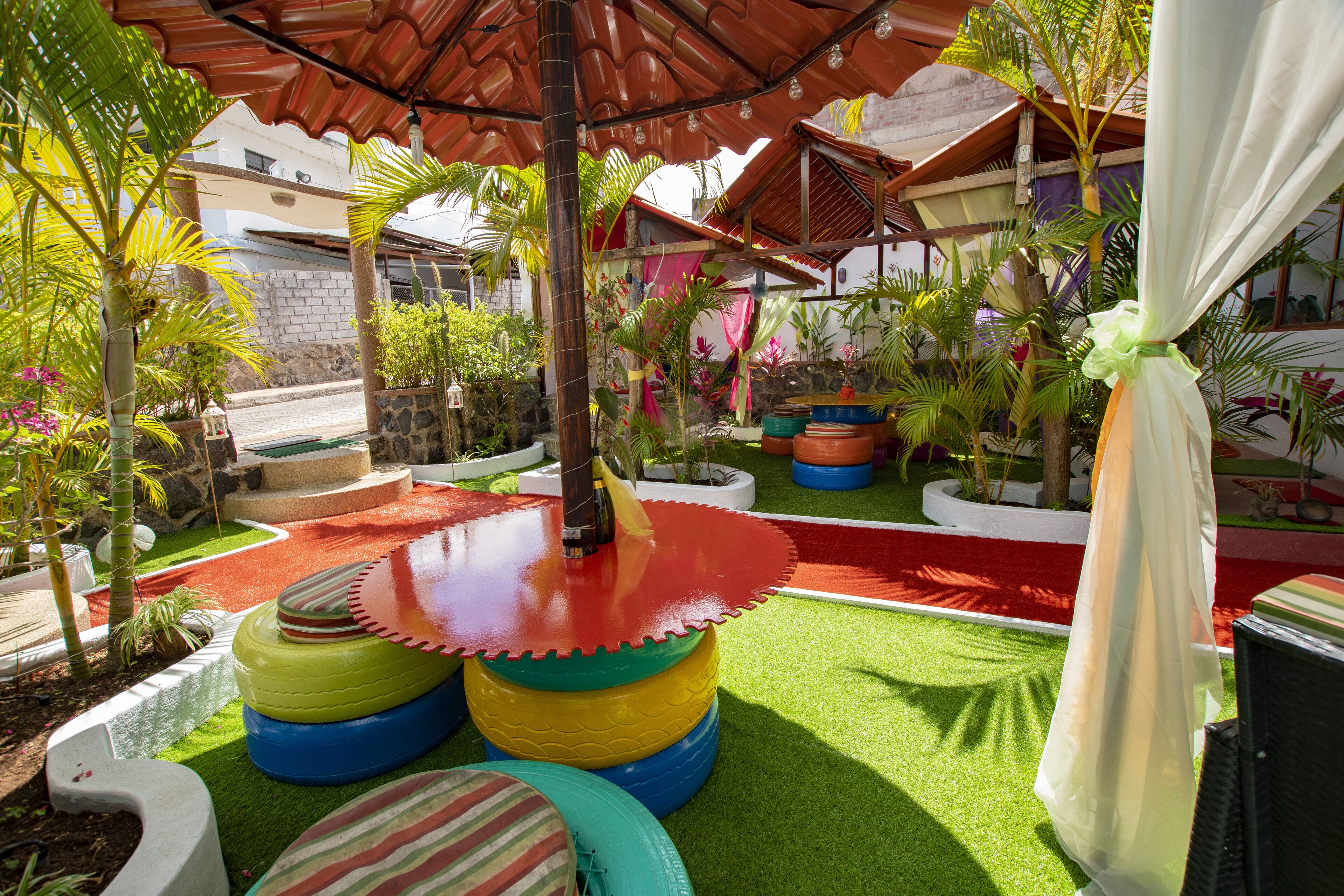 Un jardin tropical avec une pelouse artificielle, des sièges colorés faits de pneus recyclés et diverses plantes.