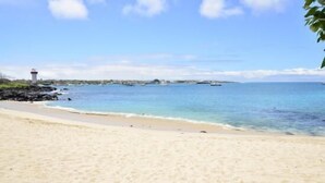 A beach with clear blue water, a lighthouse, and a rocky shoreline. - Hostal Gosén (Puerto Baquerizo Moreno)