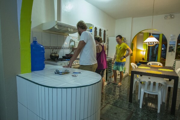 A kitchen with a stove, a large blue water bottle, and a dining area with a table and chairs. - Hostal Gosén (Puerto Baquerizo Moreno)