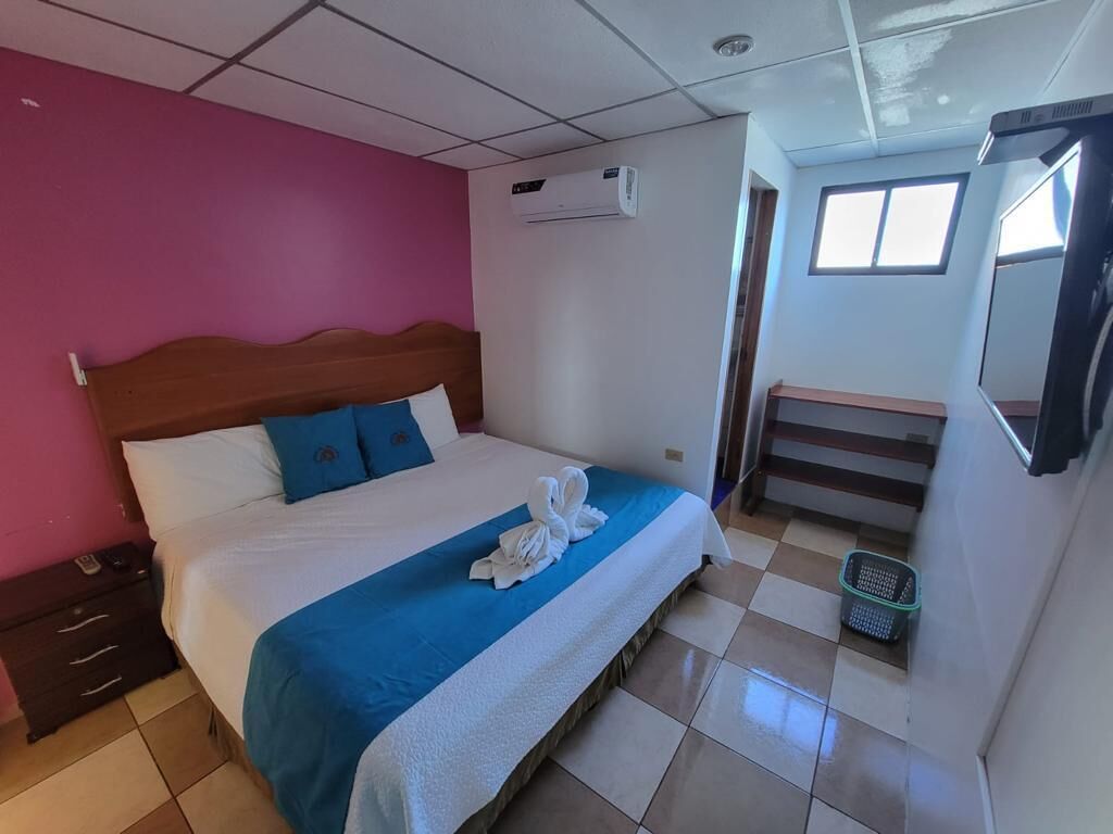 A hotel room with a bed, a wooden headboard, a blue bedspread, and a pair of towels on the bed.