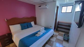 A hotel room with a bed, a wooden headboard, a blue bedspread, and a pair of towels on the bed.
