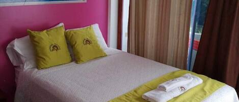 Una cama con una colcha blanca y verde, dos almohadas y una toalla doblada sobre la cama.