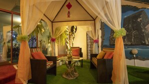 A cozy indoor setting with a glass-top table surrounded by wicker furniture, a decorative plant, and a mural on the wall. - Hostal Gosén (Puerto Baquerizo Moreno)