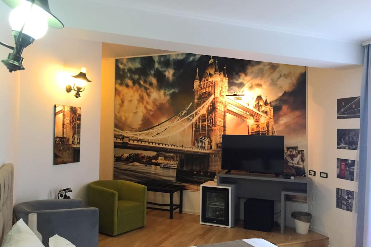 Ein Hotelzimmer mit einer großen Wandmalerei einer Brücke, einem Flachbildfernseher, einem Sofa, einem Sessel und einem kleinen Tisch.