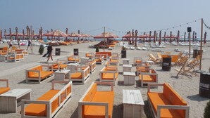 Een strand met rijen oranje en witte ligbedden en parasols.