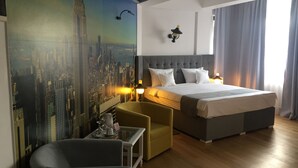 Een hotelkamer met een bed, een stoel, een klein tafeltje en een stadsgezicht muurschildering.