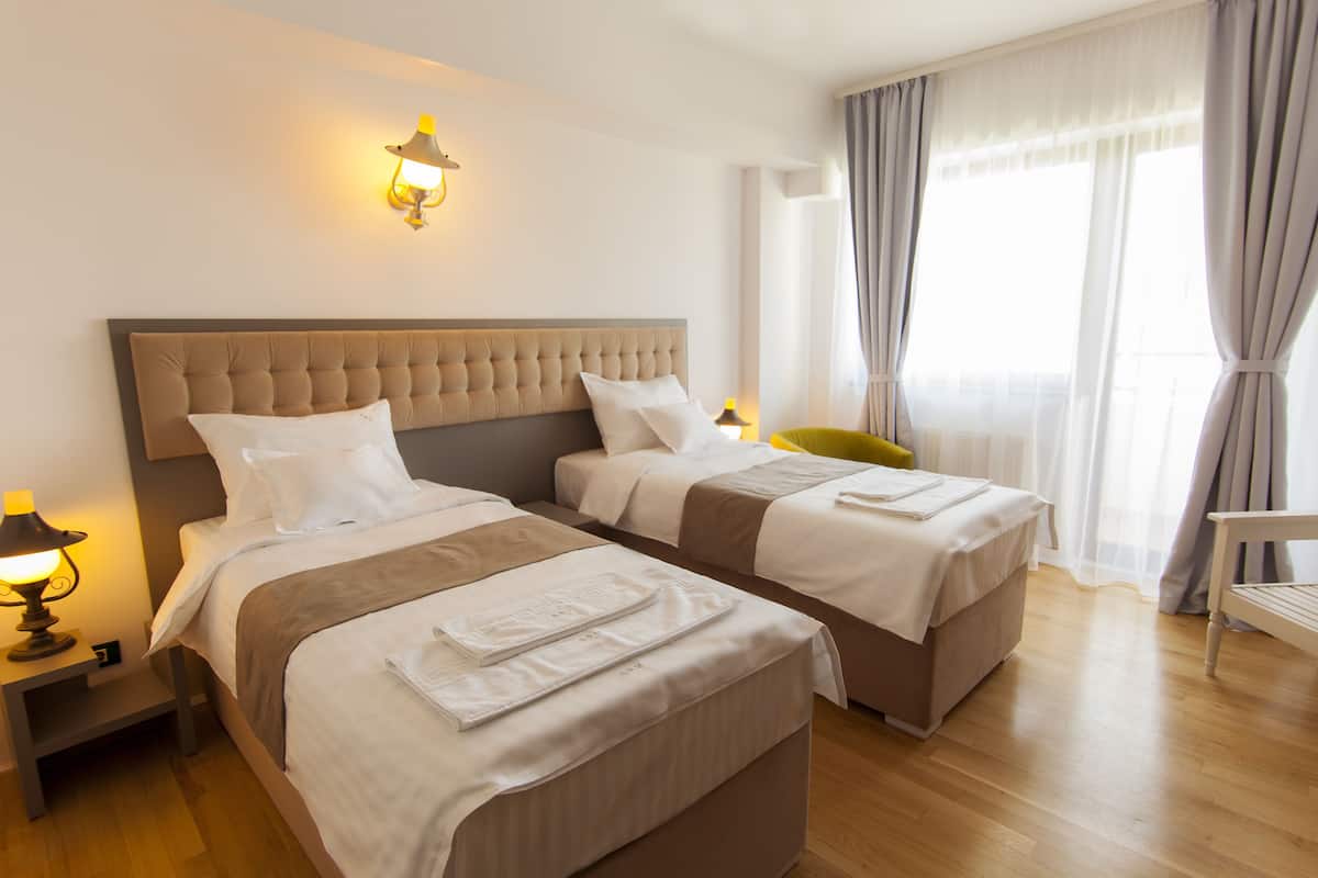 Ein Hotelzimmer mit zwei Betten, einem Nachttisch mit Lampe und einem Fenster mit Vorhängen.