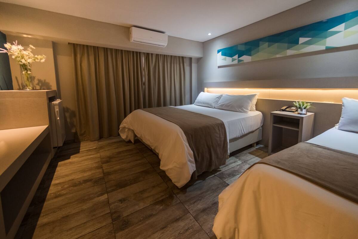 A hotel room with a bed, bedside table, and a wall-mounted air conditioner.