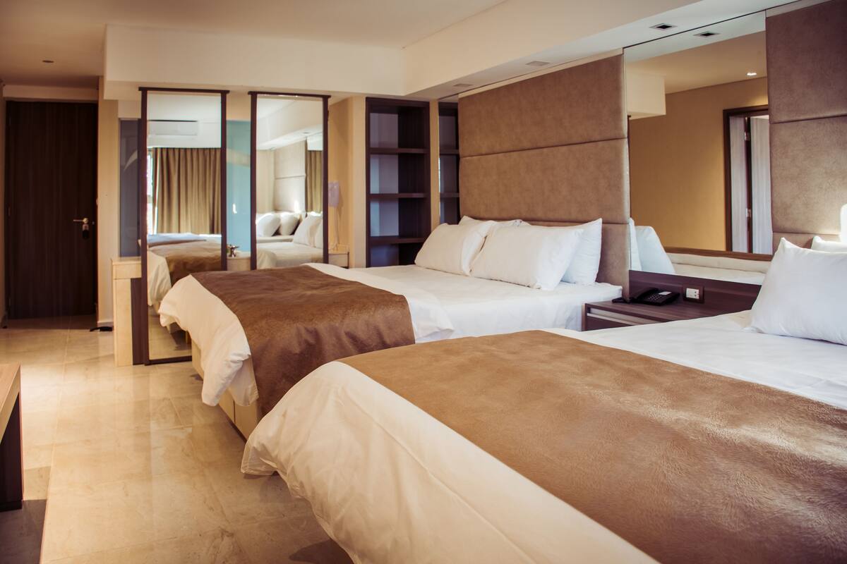 A hotel room with two beds, a large mirror, a wardrobe, and a bedside table with a lamp.
