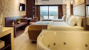 Habitación de hotel con una cama grande, una zona de estar con escritorio, una bañera amplia y un balcón con vistas.
