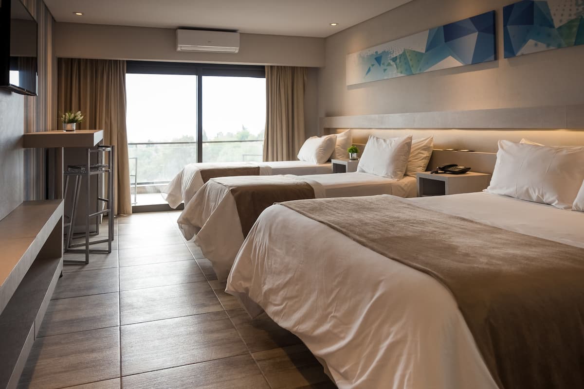 A hotel room with two beds, a desk, and a view of the outdoors.