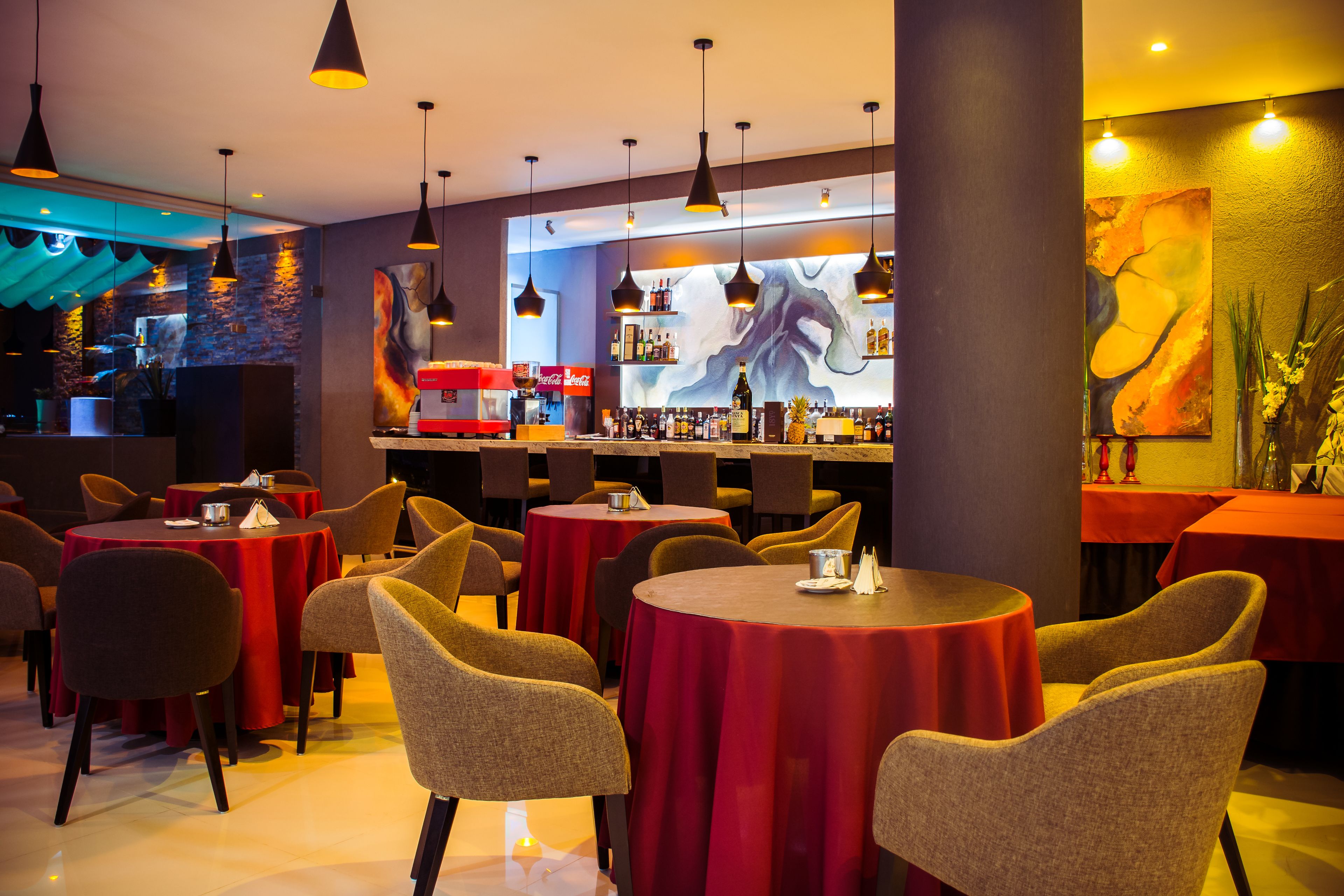 Un restaurante con mesas redondas cubiertas con manteles rojos, sillas e iluminación colgante.