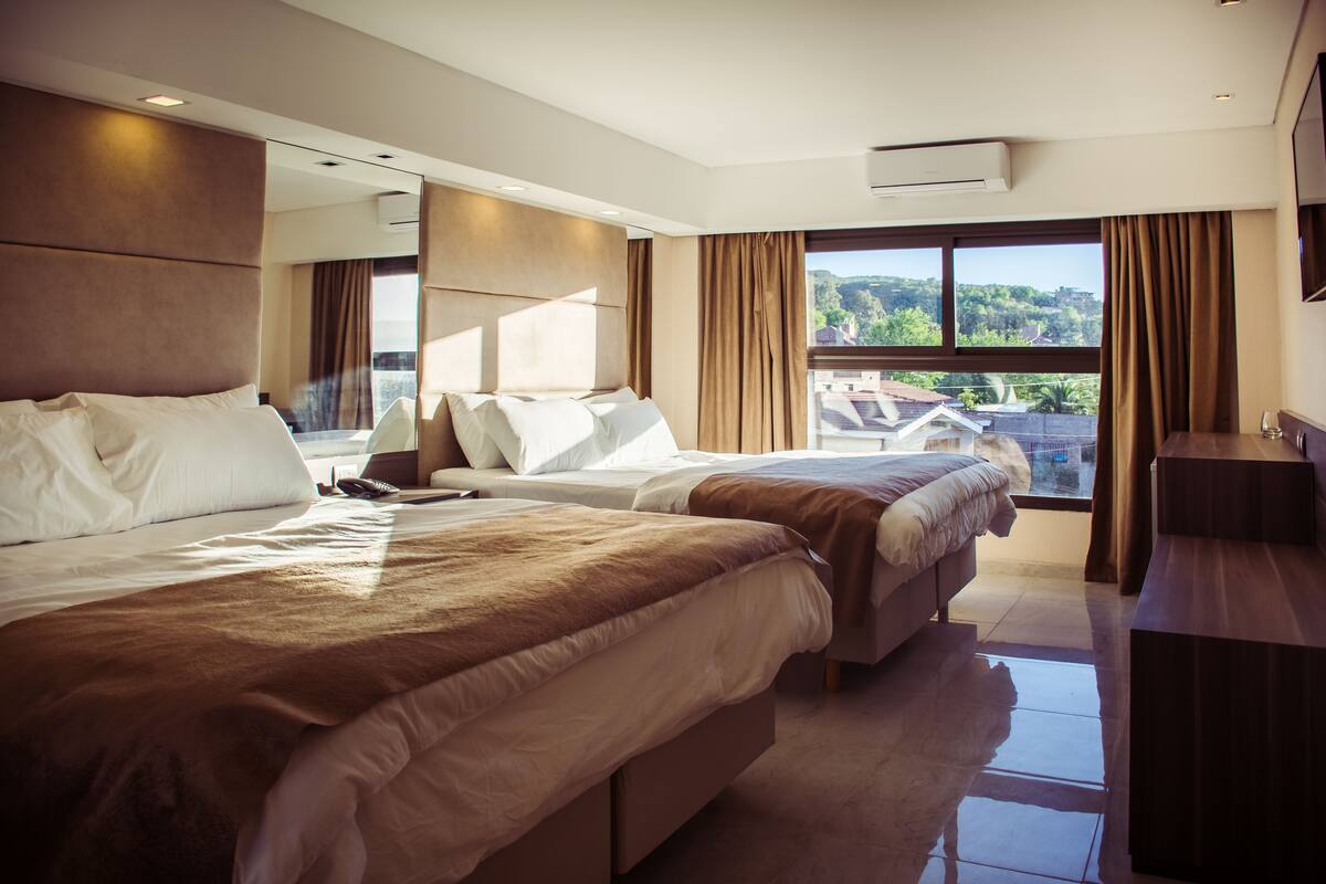 A modern hotel room with two beds, a large window with a view, and a flat-screen TV.
