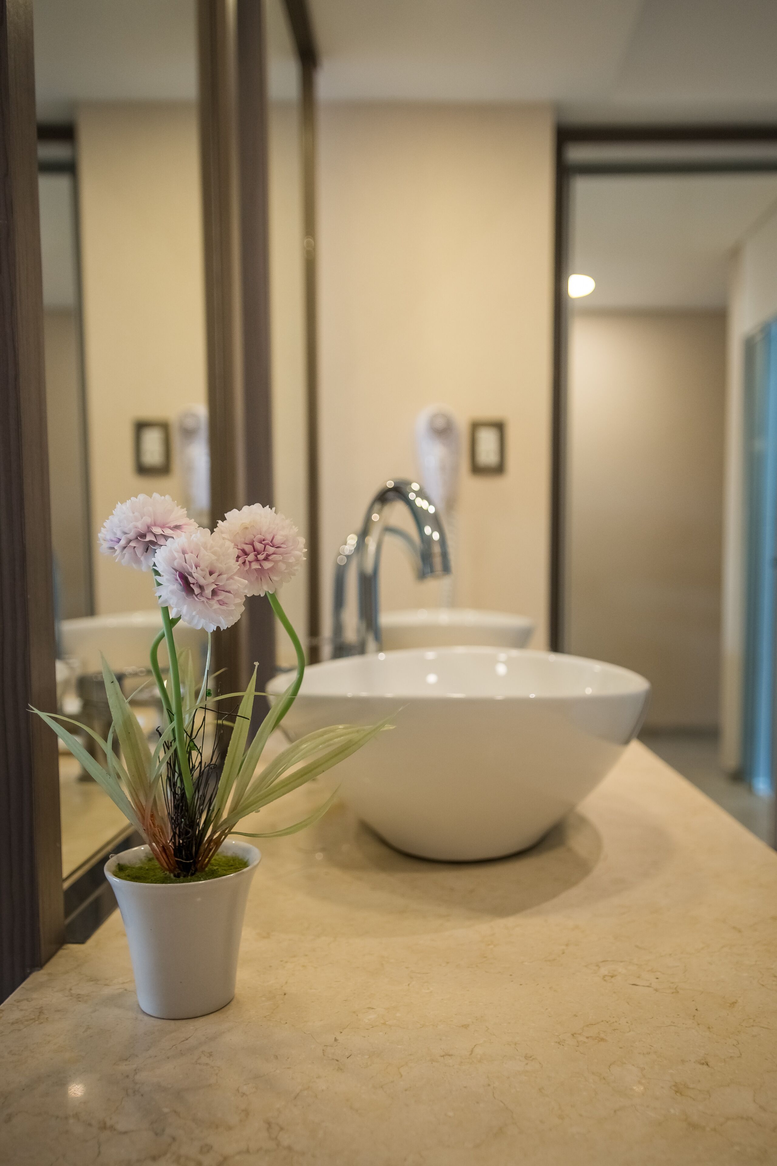 Un baño con un lavamanos blanco, un espejo y una planta en maceta con flores.