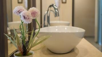 Un baño con un lavamanos blanco, un espejo y una planta en maceta con flores.