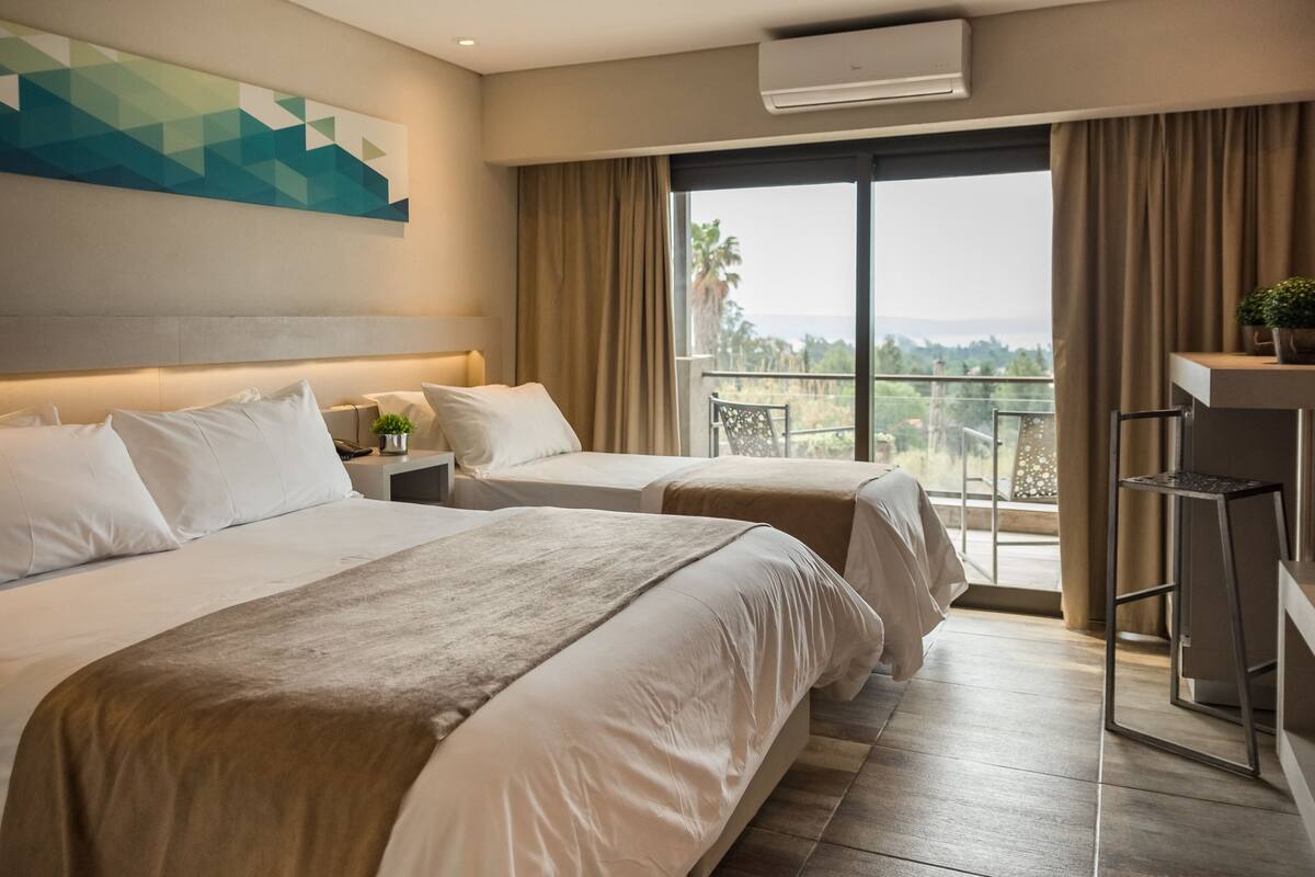 A hotel room with two beds, a balcony with a view, and a desk with a chair.