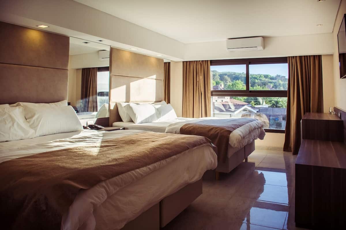 Ein Hotelzimmer mit zwei Betten, einem Schreibtisch, einem großen Fenster mit Vorhängen und einer Klimaanlage.