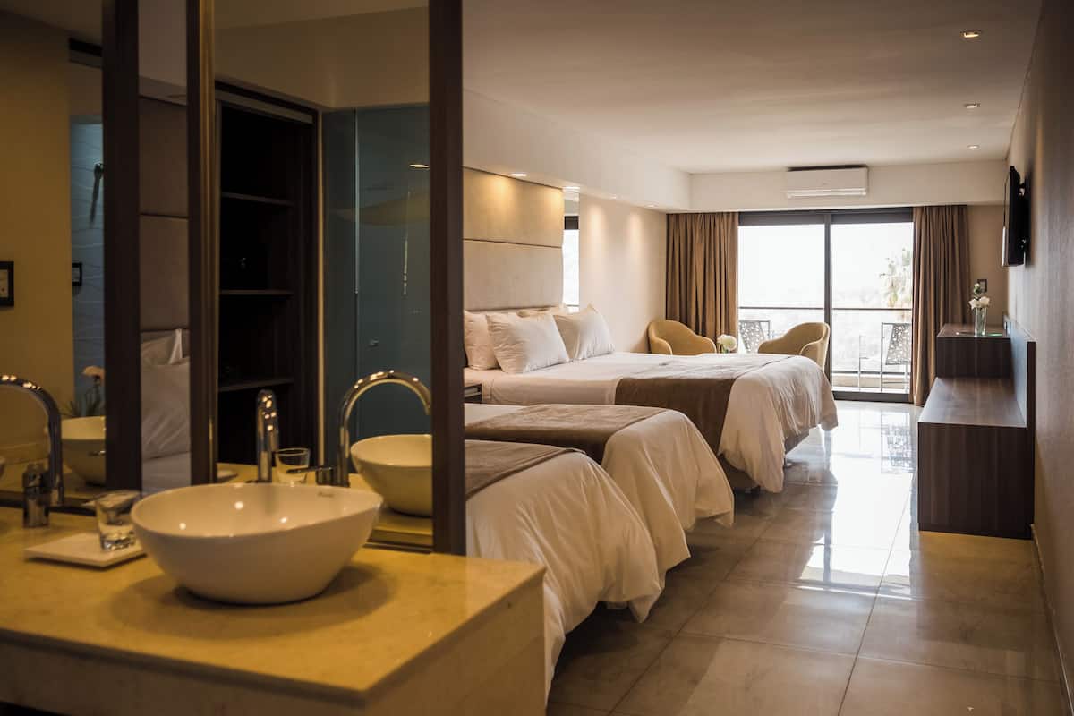 A hotel room with a large bed, a bedside table, a bathroom with a sink and mirror, and a balcony with a view.