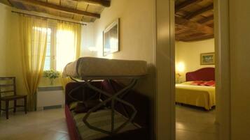 Una habitación con una cama, una silla y una mesa. Hay una ventana con cortinas, un cuadro en la pared y un techo de madera.