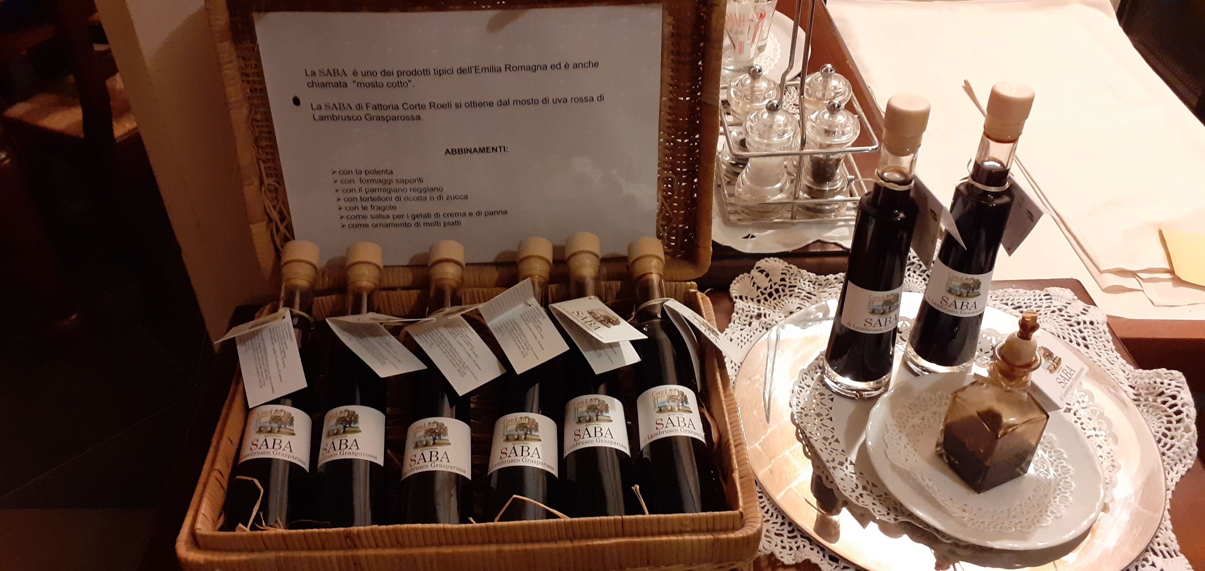 Una selección de botellas de vino SABA en una caja de madera, junto con un menú que detalla diferentes maridajes gastronómicos.