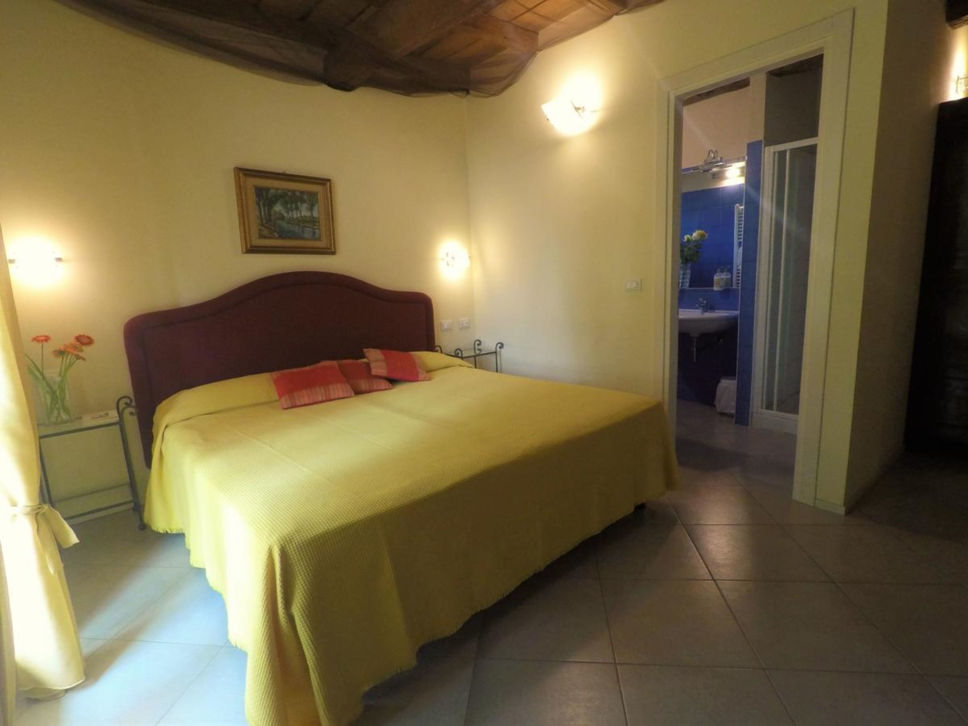 Une chambre à coucher avec un lit, des tables de chevet, un tableau encadré au mur et une salle de bain visible à travers une porte ouverte.