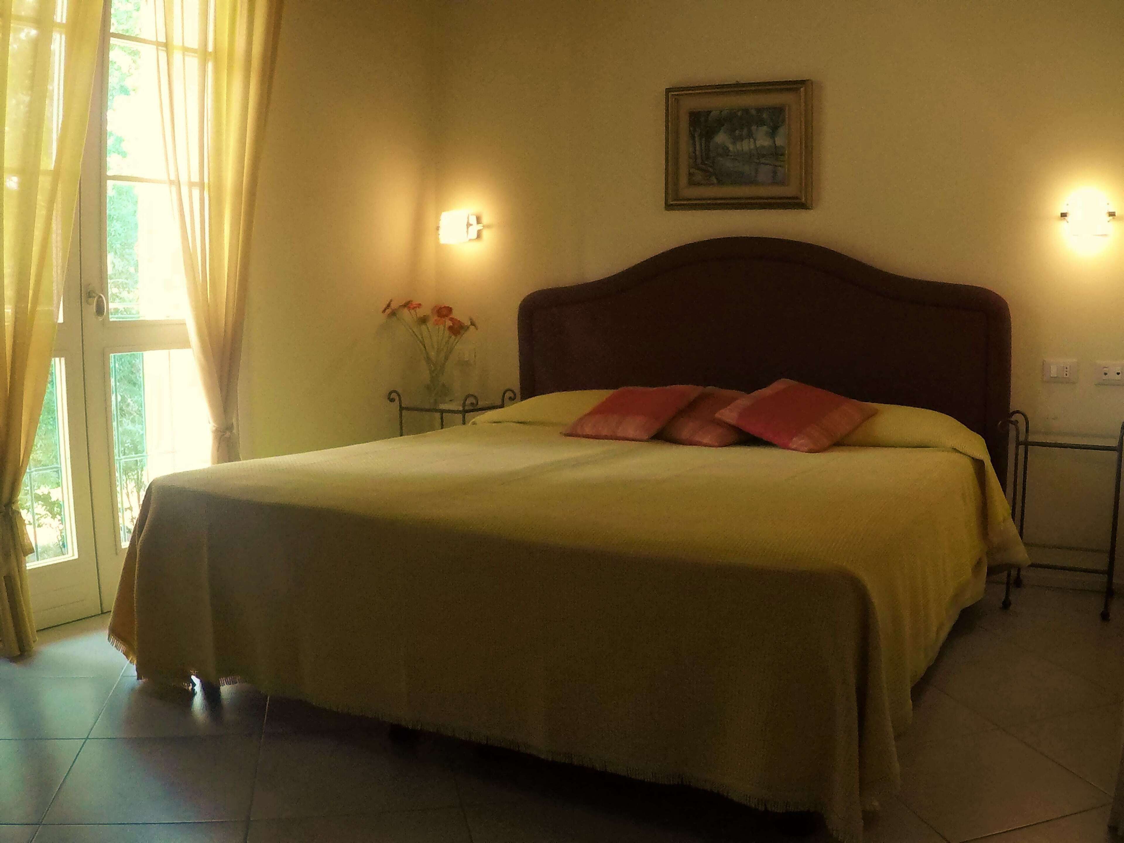 A bedroom with a bed, a nightstand, a vase with flowers, and a painting on the wall.