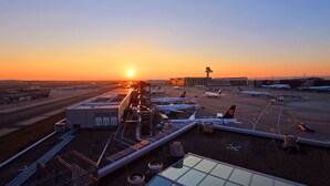 Una terminal de aeropuerto con varios aviones estacionados, cielo despejado y un atardecer al fondo.