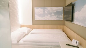 Una cama bien hecha con ropa de cama blanca, un control remoto en una mesita de noche y un televisor montado en la pared sobre la cama.