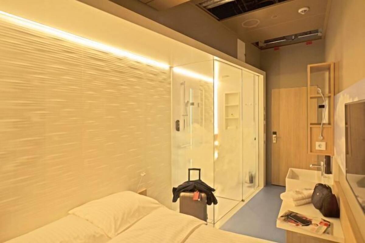 Ein Hotelzimmer mit Bett, Nachttisch, Spiegel, Kleiderschrank und kleinem Schreibtisch mit Stuhl.