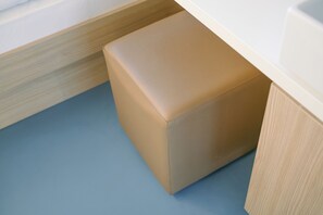 Huoneen nurkka, jossa on vaaleansininen lattia, beigenvärinen pehmustettu penkki ja puinen kaappi.