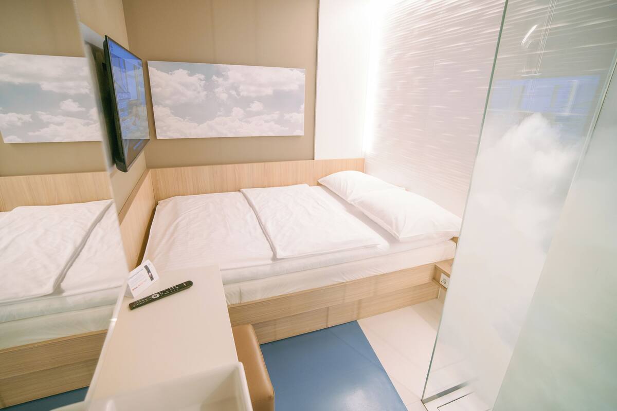 Ein Hotelzimmer mit zwei Betten, einem kleinen Tisch mit einer Fernbedienung und einer Glastrennwand.