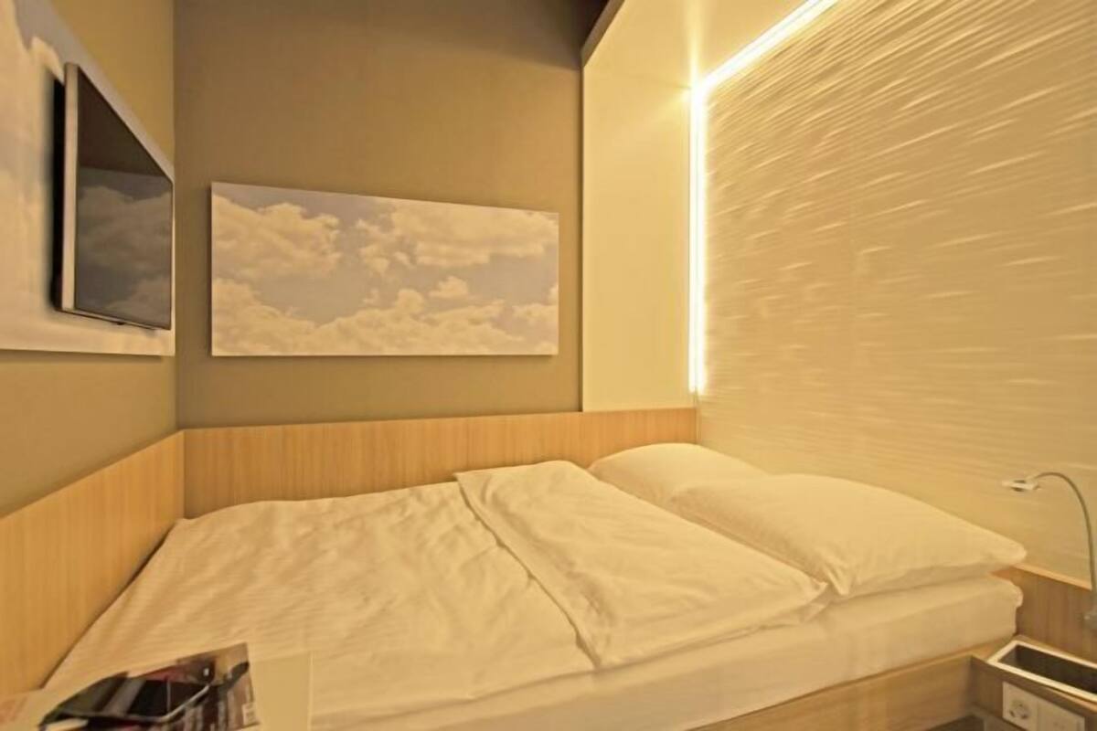 Ein Hotelzimmer mit Bett, Wandfernseher, gerahmtem Bild und Nachttisch.
