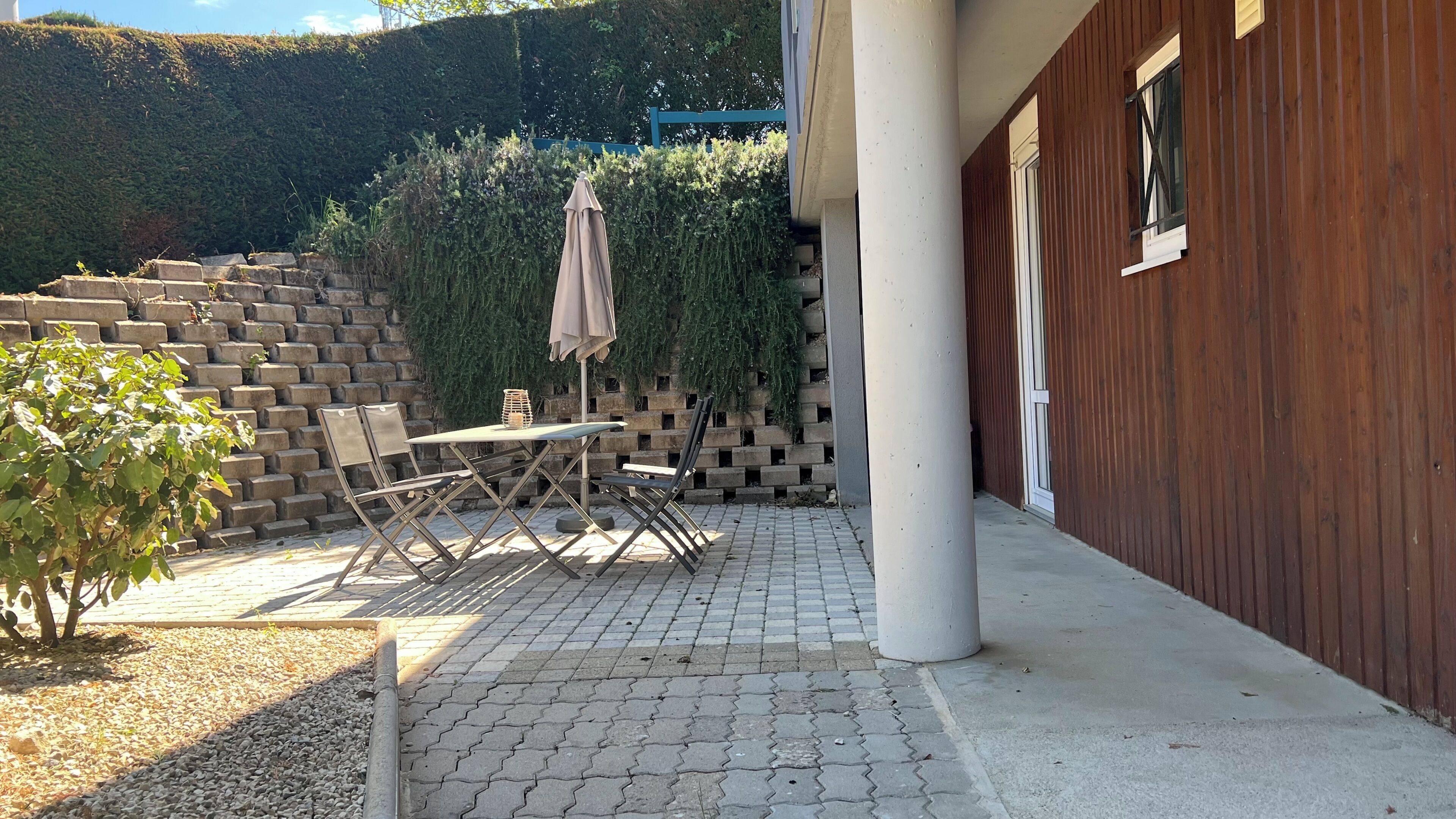 En terrasse med et bord, stole, en lille plante og en trævæg.