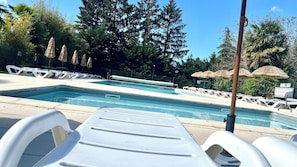 A swimming pool with lounge chairs and umbrellas, surrounded by trees and a fence.